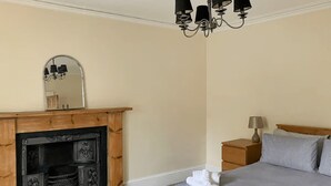 A bedroom with a fireplace, a bed with pillows, a nightstand with a lamp, and a mirror on the wall. - A quirky 2-bedroom town house just out of the centre of Tain. (Tain)