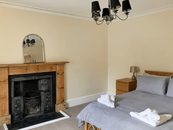 A bedroom with a fireplace, a bed with pillows, a nightstand with a lamp, and a mirror on the wall.