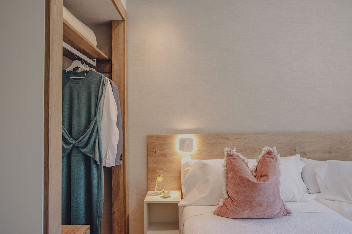 Ein Hotelzimmer mit einem Holzkopfteil, einem Nachttisch mit Lampe und einem Bett mit weißer Bettwäsche und einem rosafarbenen Kissen.