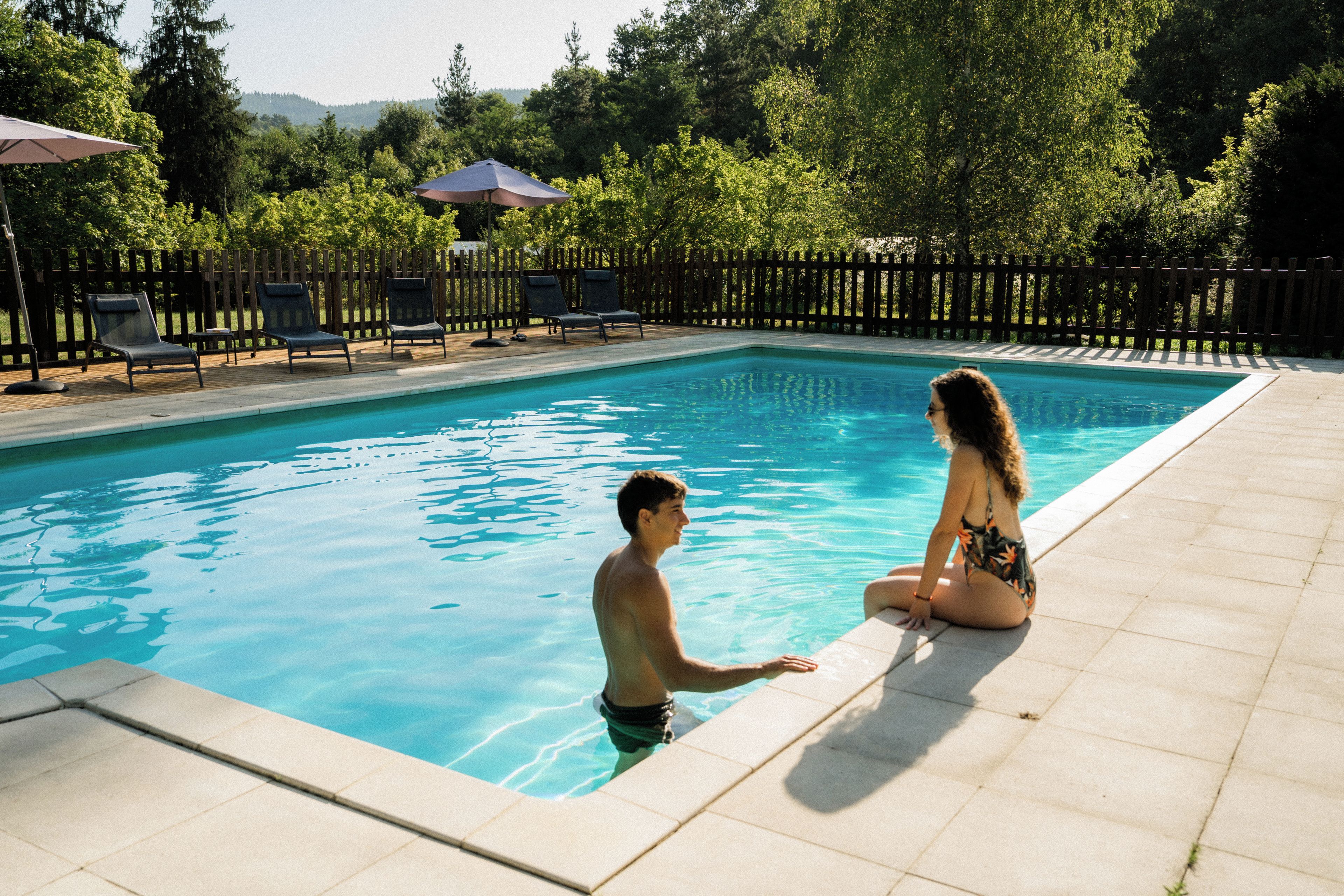 Piscina com deck de azulejos, cercada por um muro de madeira e árvores.