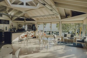 Un café moderno con techo alto, distribución abierta y amplios ventanales que ofrecen vistas al exterior.