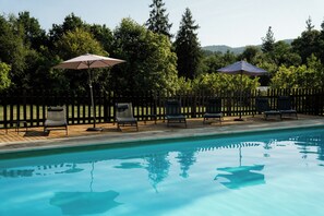 A swimming pool with lounge chairs and umbrellas, surrounded by a wooden deck and a wooden fence. - Amalurra Ecohotel & Retreat Center (Artzentales)