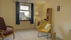 Une pièce avec une grande fenêtre, un lampadaire, une bibliothèque et un fauteuil.