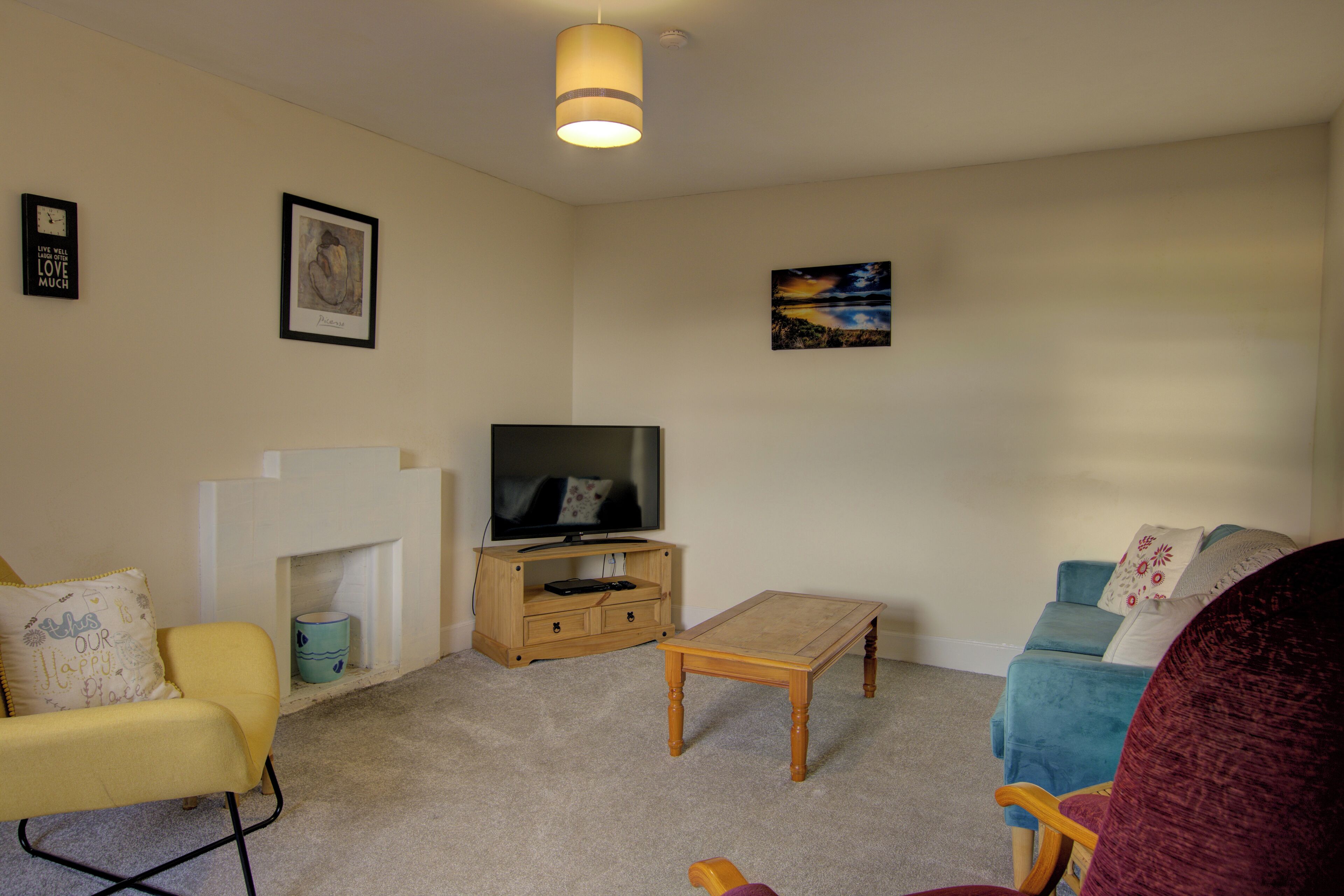 A living room with a television, a fireplace, a yellow armchair, a blue sofa, and a red chair.