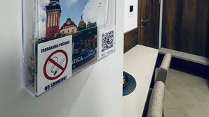 Una habitación con una mesa de comedor, sillas, una puerta de madera y un letrero en la pared con un código QR y un símbolo de prohibido fumar.
