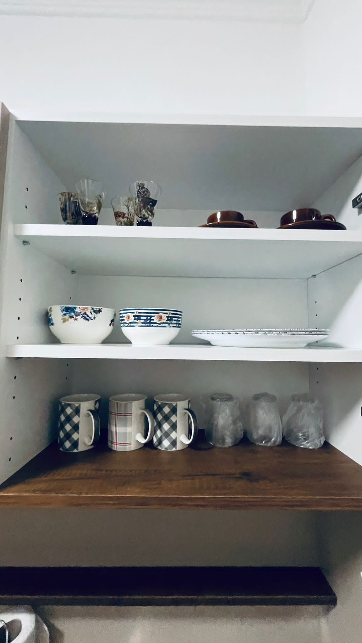 A kitchen shelf with various items including bowls, mugs, and jars.