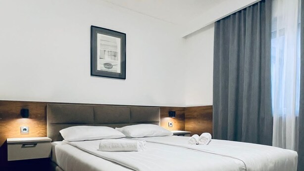 Una habitación de hotel moderna con una cama grande, dos mesitas de noche, un cuadro enmarcado en la pared y una ventana con cortinas.