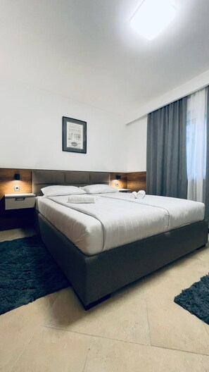 Une chambre d’hôtel moderne avec un grand lit, deux tables de chevet, un tableau encadré au mur et une fenêtre avec des rideaux.