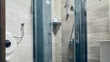 Klassieke driepersoonskamer | Badkamer | Een douche, een haardroger, handdoeken, zeep