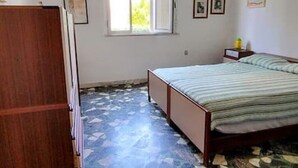 Un dormitorio con cama, un armario de madera, un ventanal y una mesita de noche con lámpara.