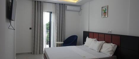 A hotel room with a bed, a chair, a TV, an air conditioner, and a window with curtains.