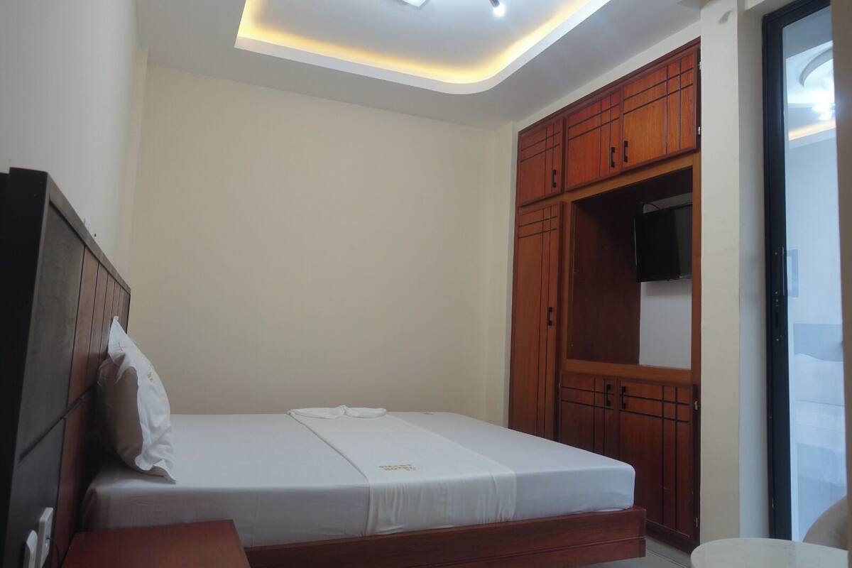 A bedroom with a bed, wooden wardrobe, and a TV.