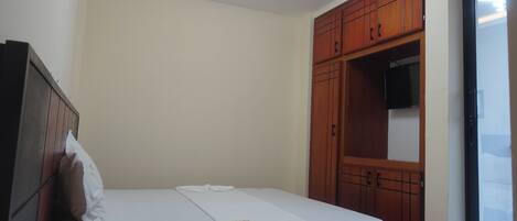 A bedroom with a bed, wooden wardrobe, and a TV.