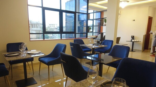 A modern dining area with blue chairs and tables, large windows with a city view, and a clean, well-lit interior. - SMART HOTEL (Douala)