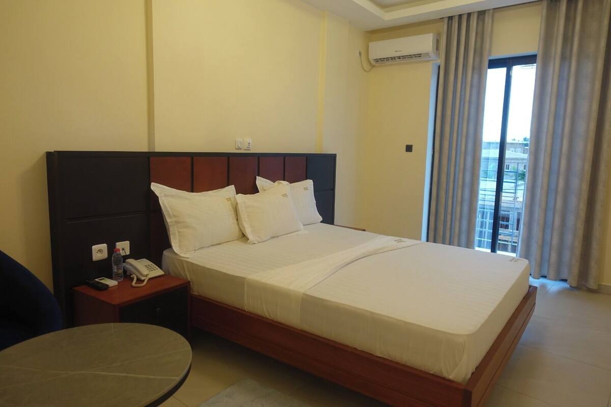 A hotel room with a bed, bedside table, and a view of the outside.