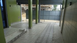 A covered outdoor area with tiled flooring, green walls, and a view of a construction site. - SMART HOTEL (Douala)