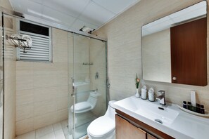 A modern bathroom with a glass shower enclosure, a white toilet, and a vanity with a mirror and toiletries. - AM Hotel Kollection: Manasa Inn, Tirupati (Tirupati)