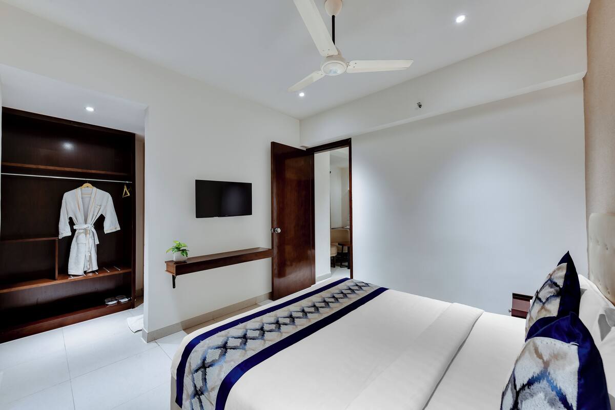 Una habitación de hotel moderna con una cama grande, un ventilador de techo, un televisor montado en la pared y un armario de madera.