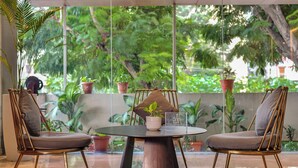 A modern outdoor seating area with two chairs and a table, surrounded by potted plants and a view of lush greenery. - AM Hotel Kollection: Manasa Inn, Tirupati (Tirupati)