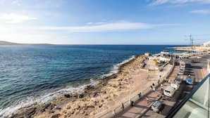 Vista costera con playa rocosa, paseo marítimo y carretera con vehículos.