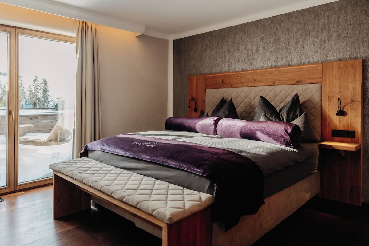 A modern bedroom with a large bed, a bench, and a view of a snowy landscape through a sliding glass door.