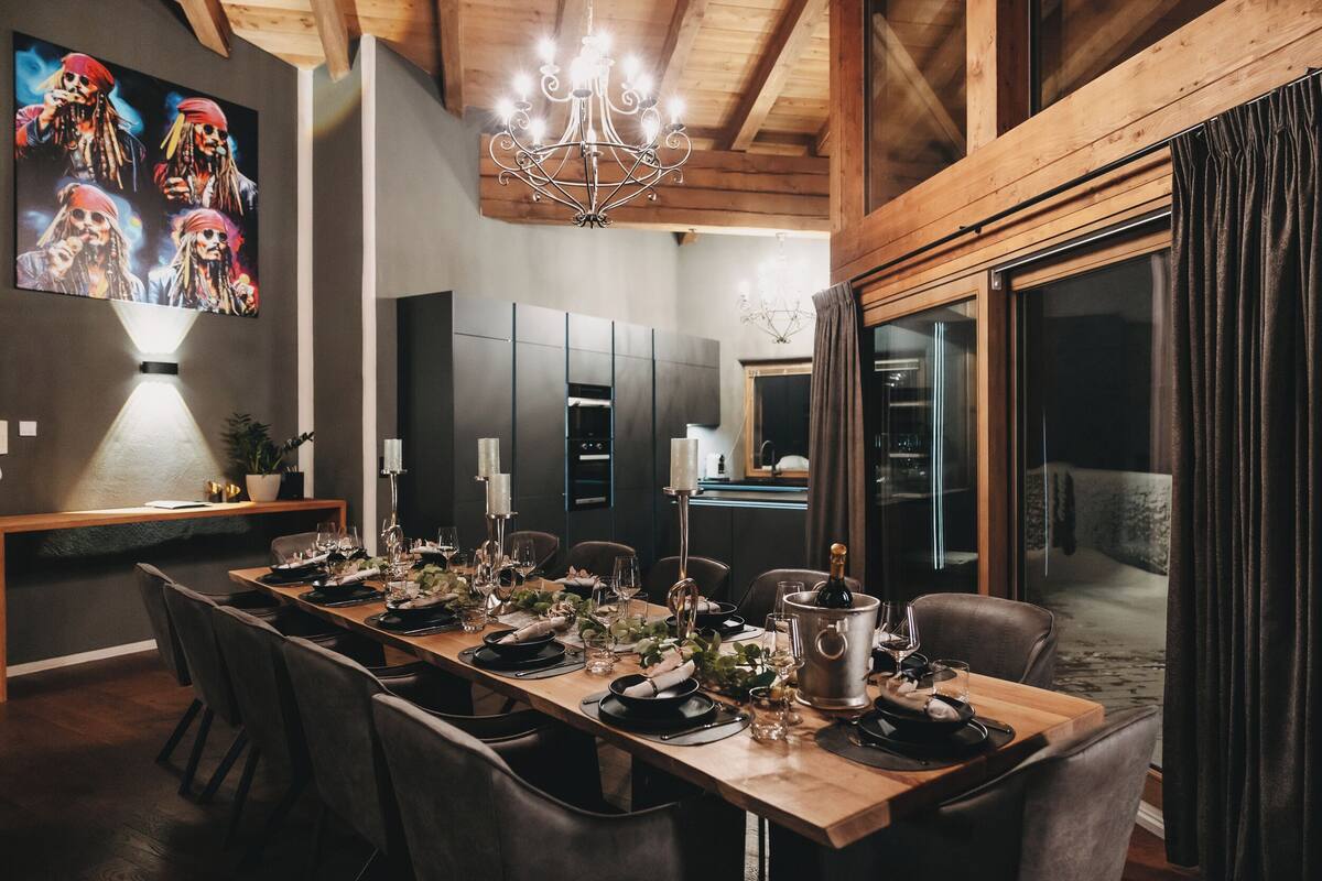 A dining area with a long wooden table set for a meal, surrounded by chairs.