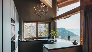 Een moderne keuken met een groot eiland, een kroonluchter en uitzicht op bergen door grote ramen.