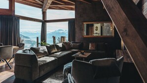 Een moderne woonkamer met een ruime hoekbank, een salontafel en uitzicht op bergen door grote ramen.
