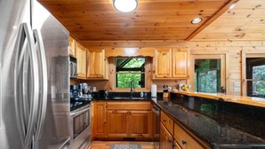 A modern kitchen with wooden cabinets, a stainless steel refrigerator, and a black countertop. - Tranquil Ridge- View, pet friendly, hot tub, sauna (Epworth)