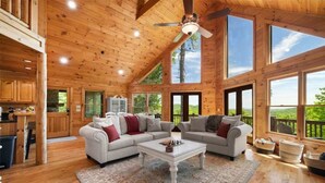 A spacious cabin with wooden walls and large windows, a dining area, and a living room with a fireplace. - Tranquil Ridge- View, pet friendly, hot tub, sauna (Epworth)