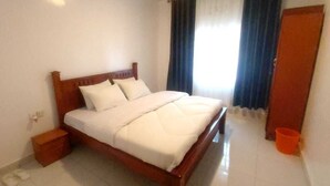 Una cama bien hecha con ropa blanca, un cabecero de madera y una mesita de noche de madera a su lado.