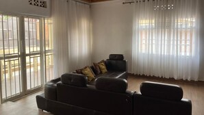 Un salón espacioso con un sofá de cuero grande, una araña y ventanas amplias con cortinas traslúcidas.