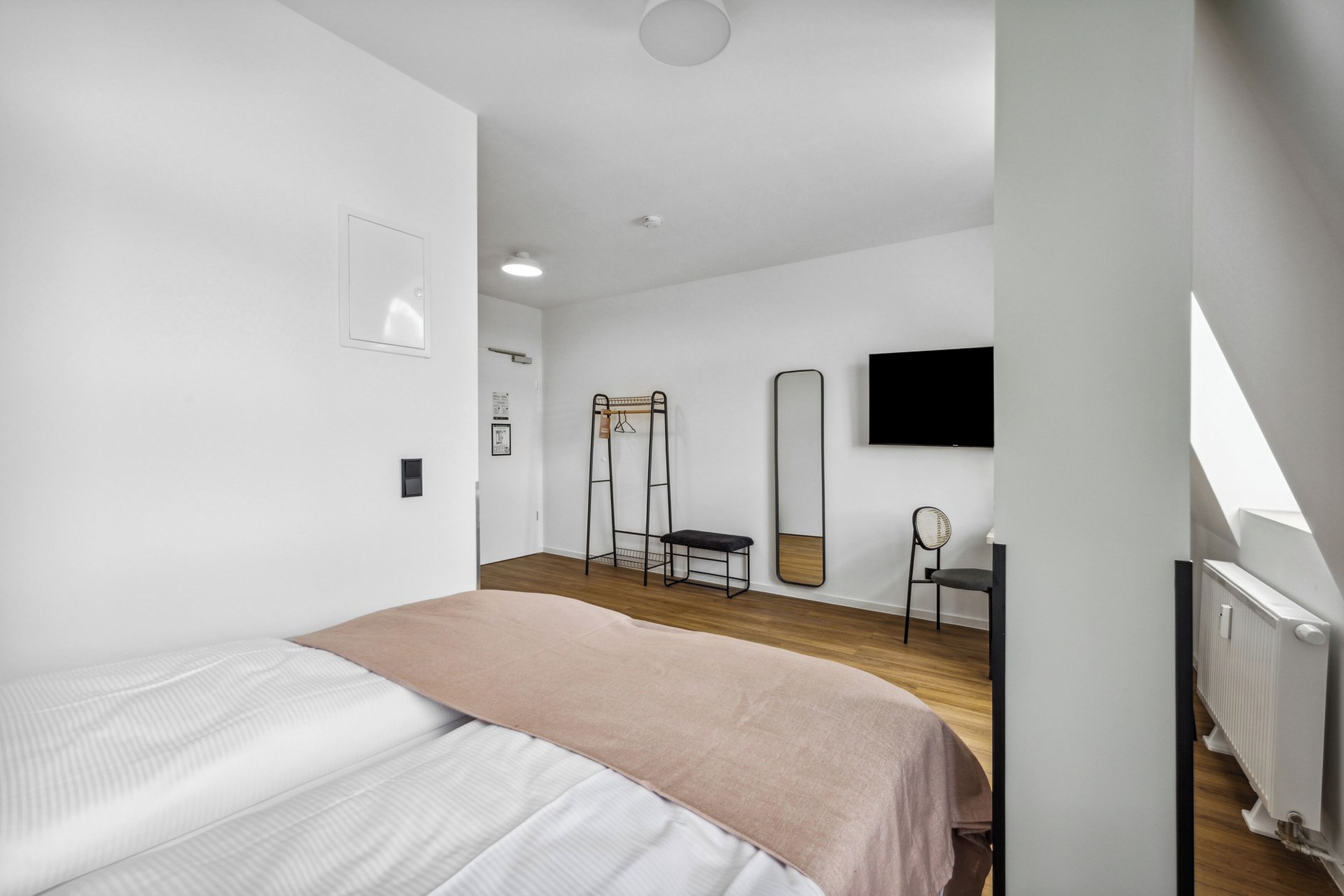 A modern bedroom with a bed, a desk, a chair, and a large mirror.