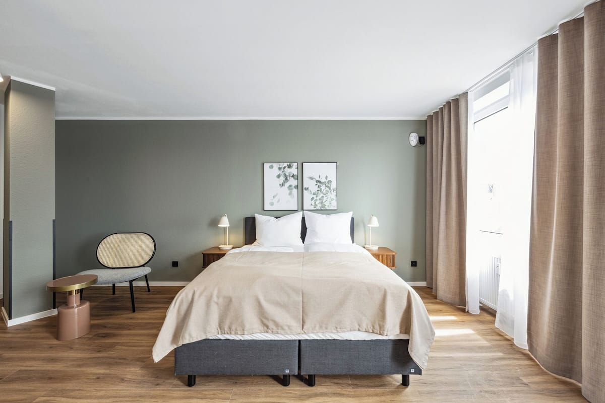 Une chambre à coucher moderne avec un grand lit, des tables de chevet, une chaise et des œuvres d’art accrochées au mur.
