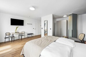 A modern hotel room with a large bed, a desk with chairs, a flat-screen TV, and a mirror. - Limehome Düsseldorf Bahlenstr. (Düsseldorf)