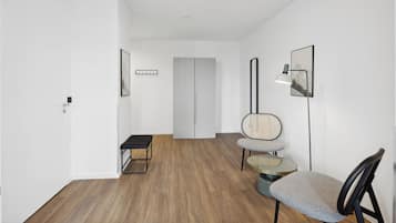 A modern, minimalist hallway with a wooden floor, a bench, a round table with a chair, and a door at the end.