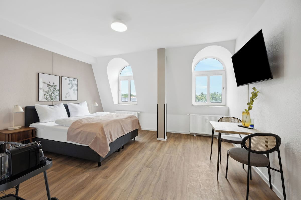 Une chambre d’hôtel moderne équipée d’un lit, d’un bureau, d’une chaise et d’un téléviseur fixé au mur.