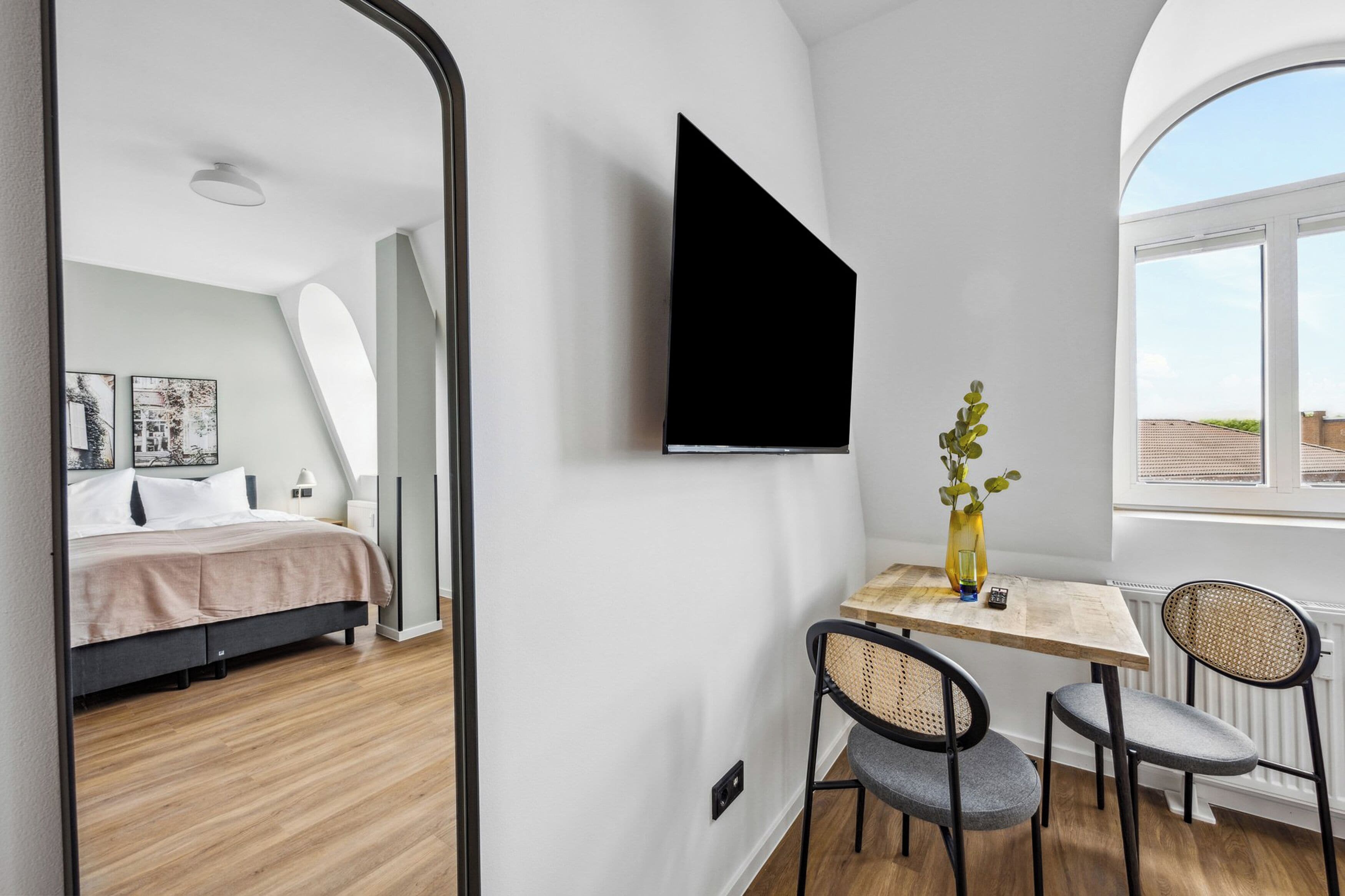 Een moderne kamer met een bed, een bureau met twee stoelen, een groot raam en een tv aan de muur.