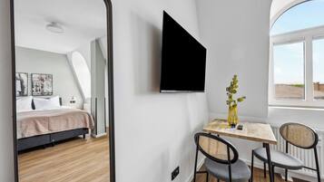 Een moderne kamer met een bed, een bureau met twee stoelen, een groot raam en een tv aan de muur.
