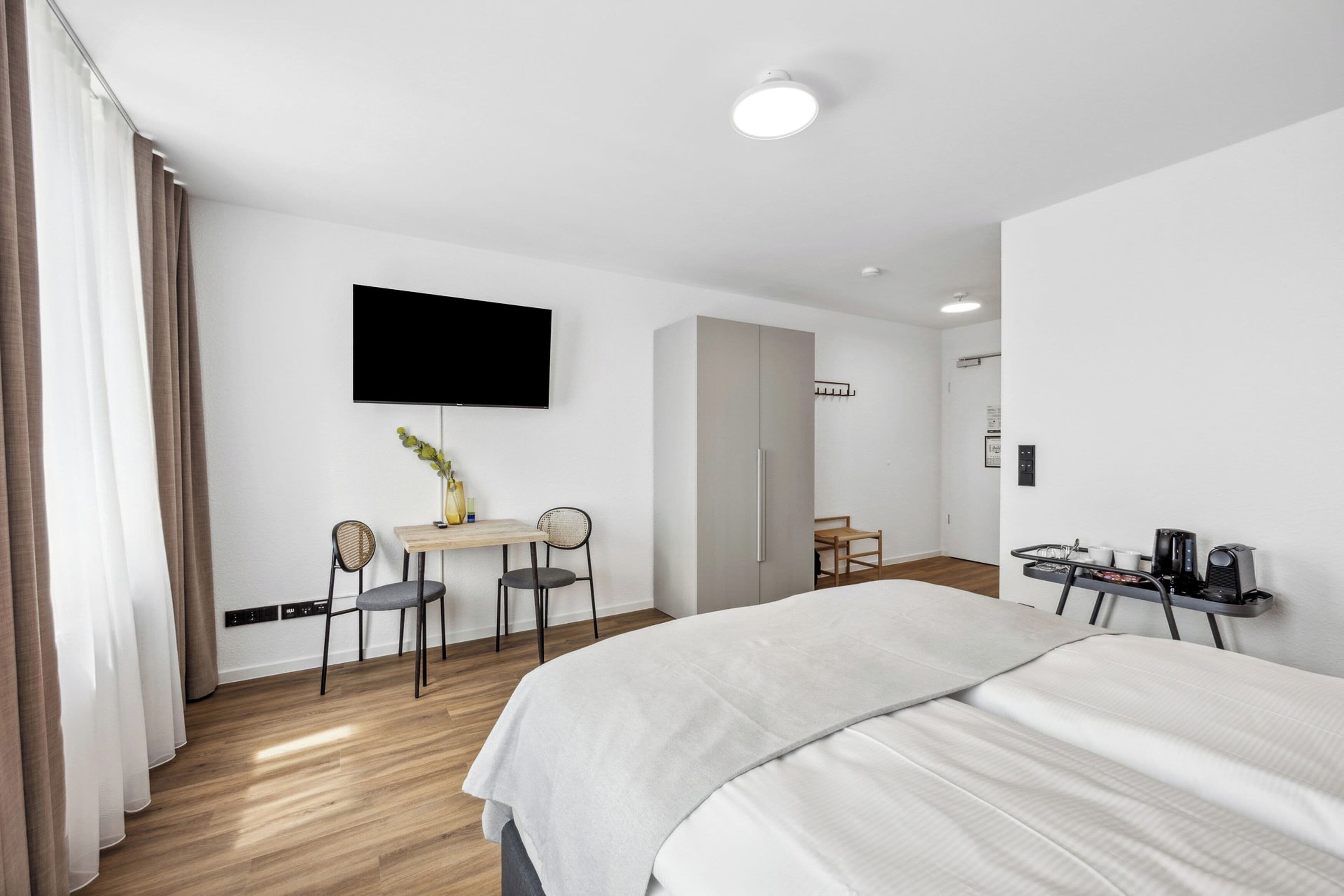 Ein Hotelzimmer mit einem Bett, einem Schreibtisch mit Stuhl, einem Flachbildfernseher und einer Kaffeemaschine.