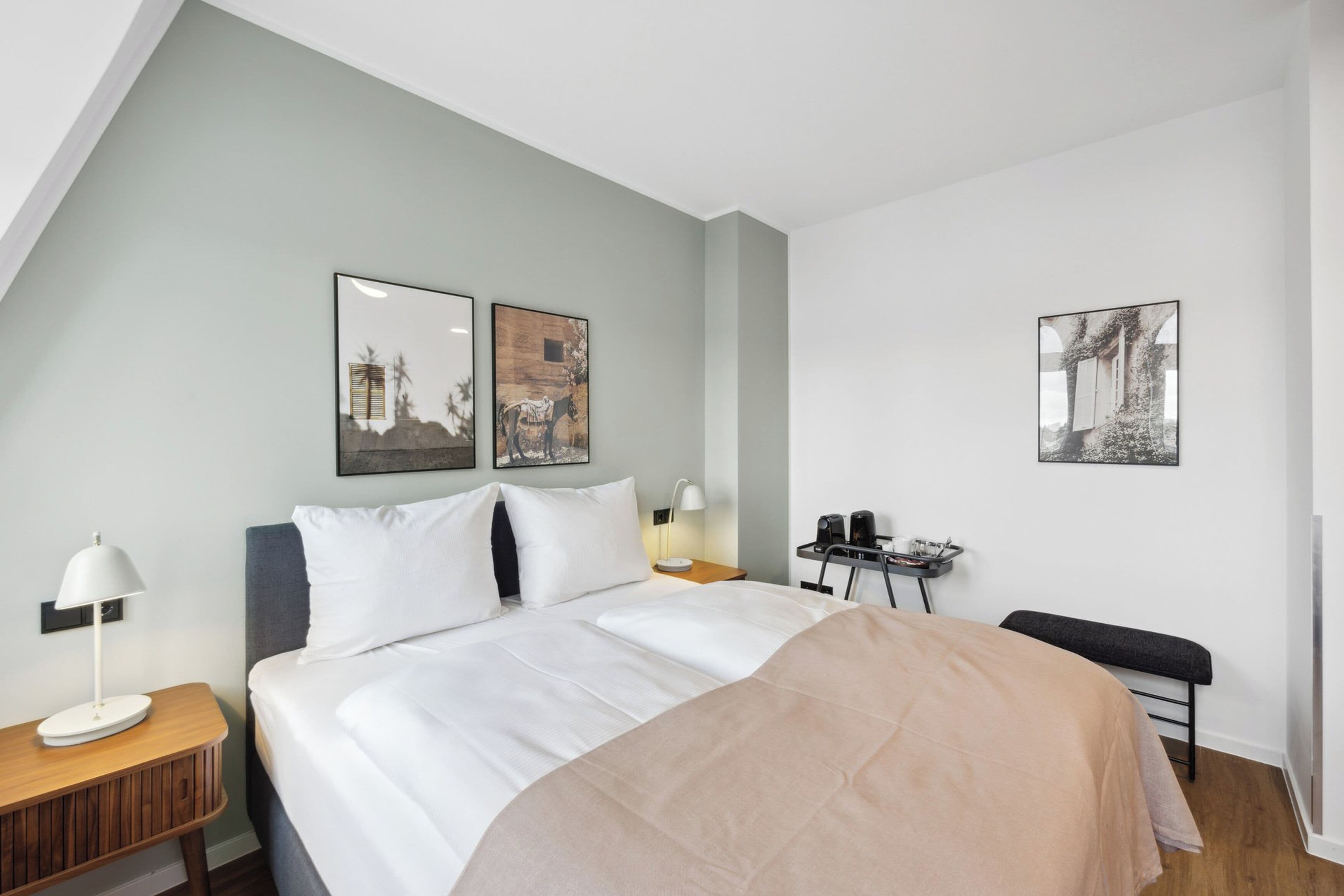 A modern hotel room with a bed, bedside tables, and artwork on the walls.