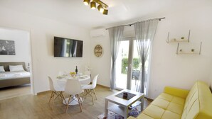 A modern living room with a yellow sofa, a dining table with chairs, a flat-screen TV, and a large window with curtains. - Villa Mares 1 with shared pool in a quiet village near Umag (Cepljani)
