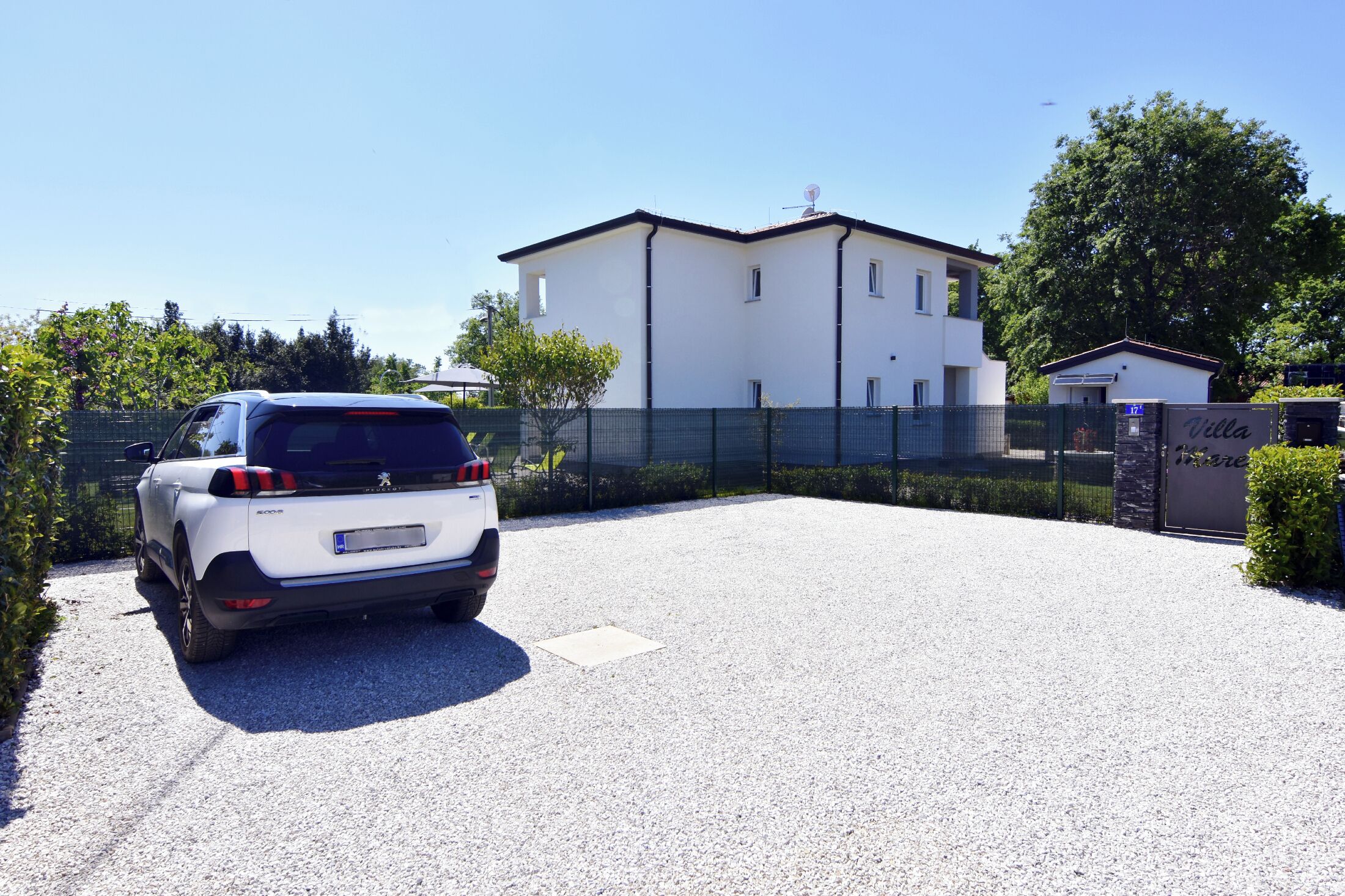 Un VUS blanc est garé sur une allée de gravier, avec un bâtiment blanc en arrière-plan.