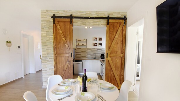 A dining area with a white table set for four, a kitchen in the background, and a sliding barn door entrance. - Villa Mares 1 with shared pool in a quiet village near Umag (Cepljani)