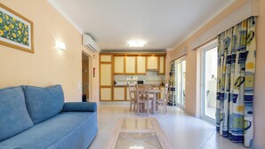 A living room with a blue sofa, a glass-top coffee table, and a kitchen in the background. - Vila Marachique - Torralvor (Portimão)