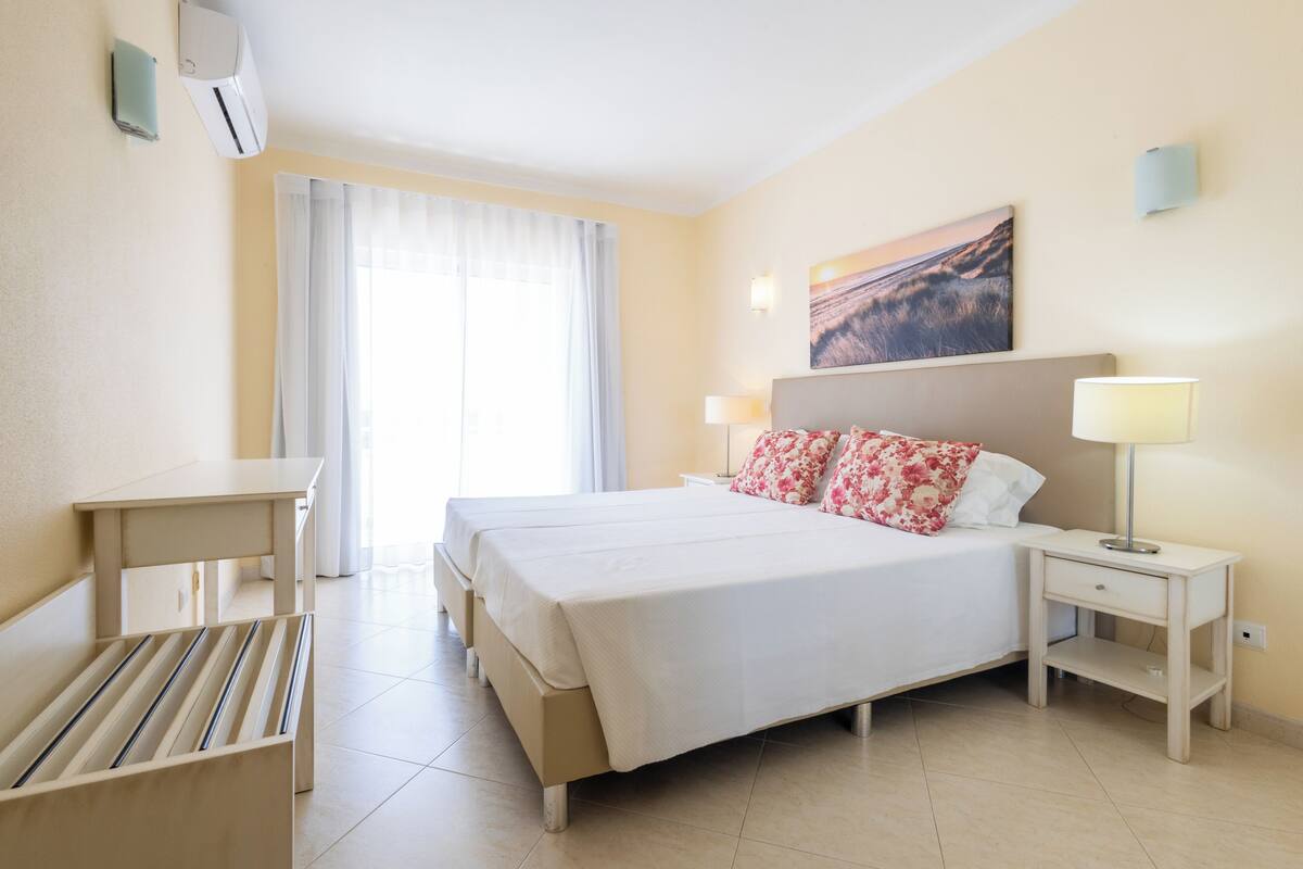 A hotel room with a bed, bedside tables, a desk, and a window with curtains.