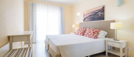 A hotel room with a bed, bedside tables, a desk, and a window with curtains.