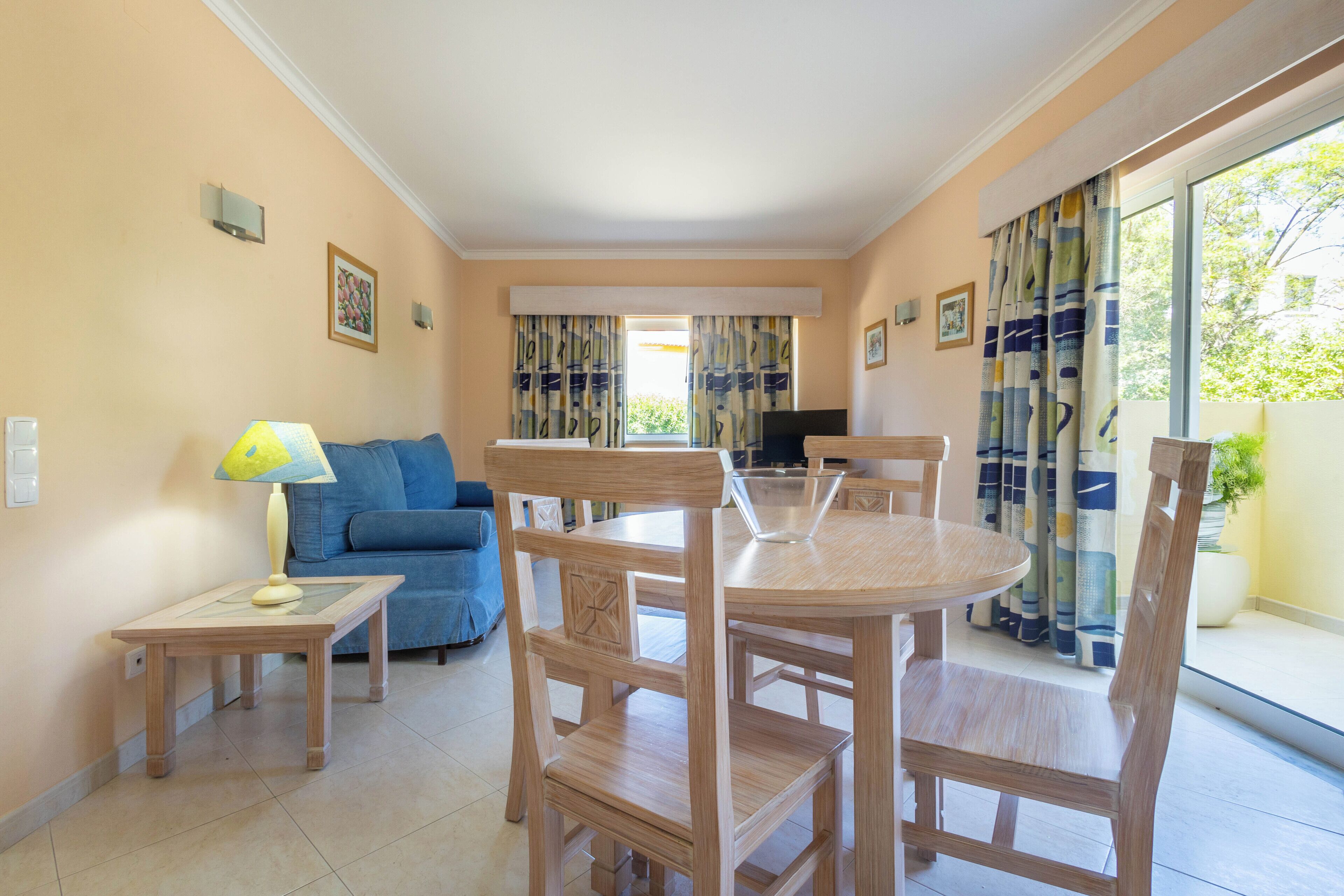Un salon avec un canapé, une table à manger avec des chaises, un téléviseur et une fenêtre avec des rideaux.