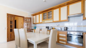 A modern kitchen with wooden cabinets, a built-in oven, and a dining table with chairs. - Vila Marachique - Torralvor (Portimão)