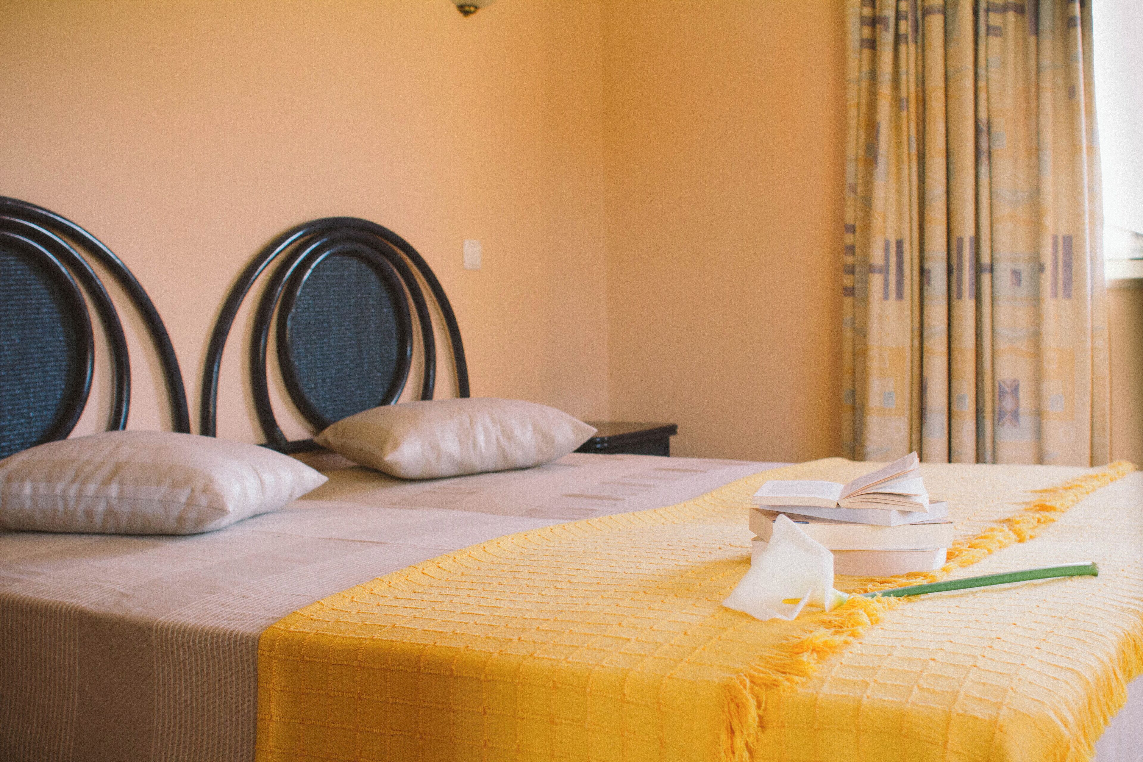 A hotel room with a bed, pillows, a bedside table, and a window with curtains.
